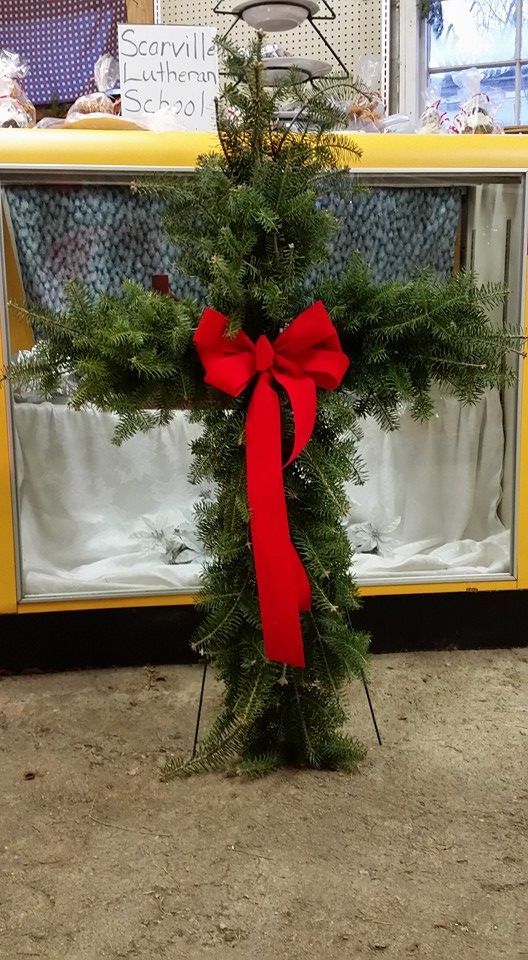 A christmas cross wreath with a red bow is leaning on a table.