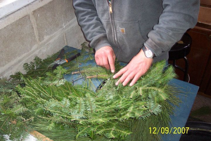 A man in a Carhartt jacket is assembling a wreath on a crimping table.