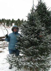 A woman is standing next to a Christmas tree in the snow.