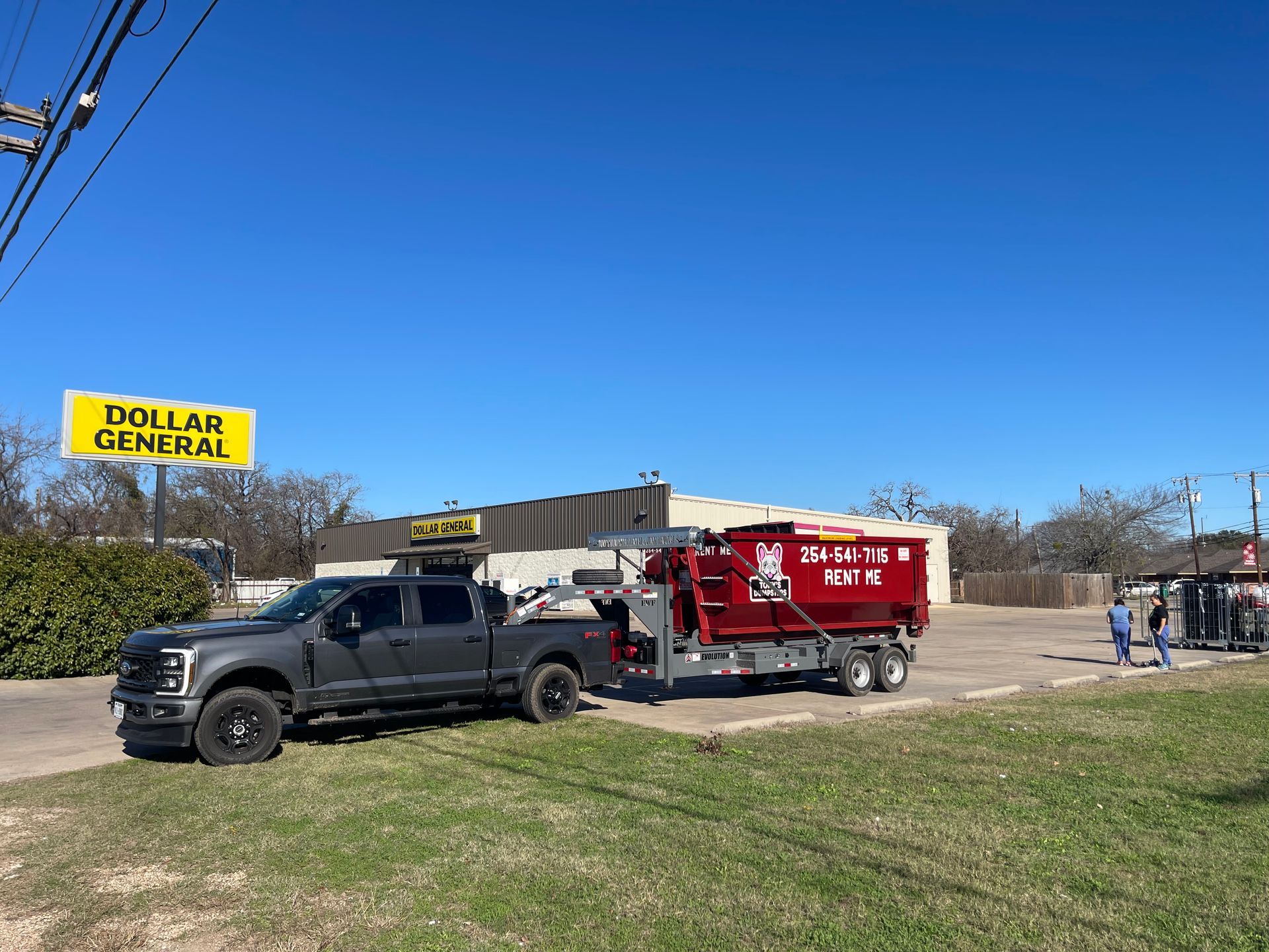 A green dumpster is parked in front of a store.