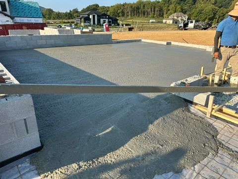 Newly poured concrete slab being leveled with a long tool at a construction site.