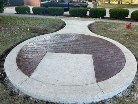Circular concrete patio with brick-patterned inset, pathway leading away.