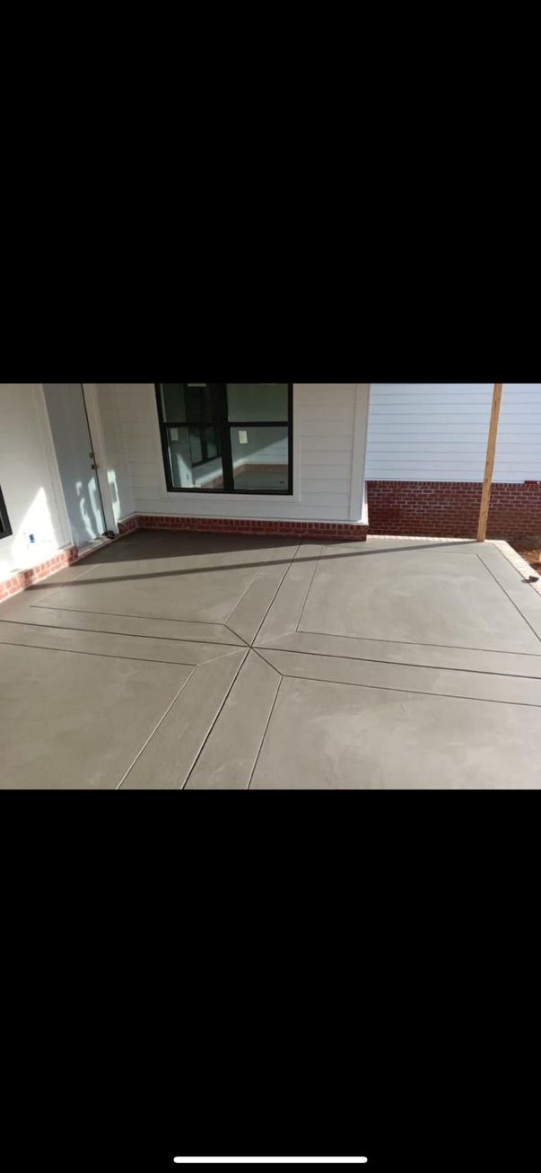 A concrete patio with grid-like score lines, next to a building with a window and white siding.