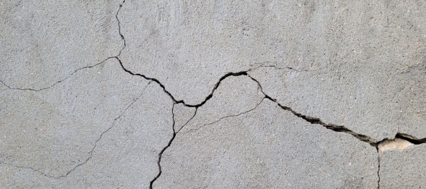Cracked concrete surface with irregular dark lines. Gray backdrop.