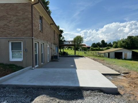 Concrete patio next to a two-story brick building, leading to a wooden deck, with a barn in the background.