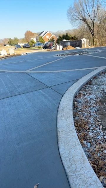 Newly poured concrete driveway with decorative border. Houses and trees in the background.