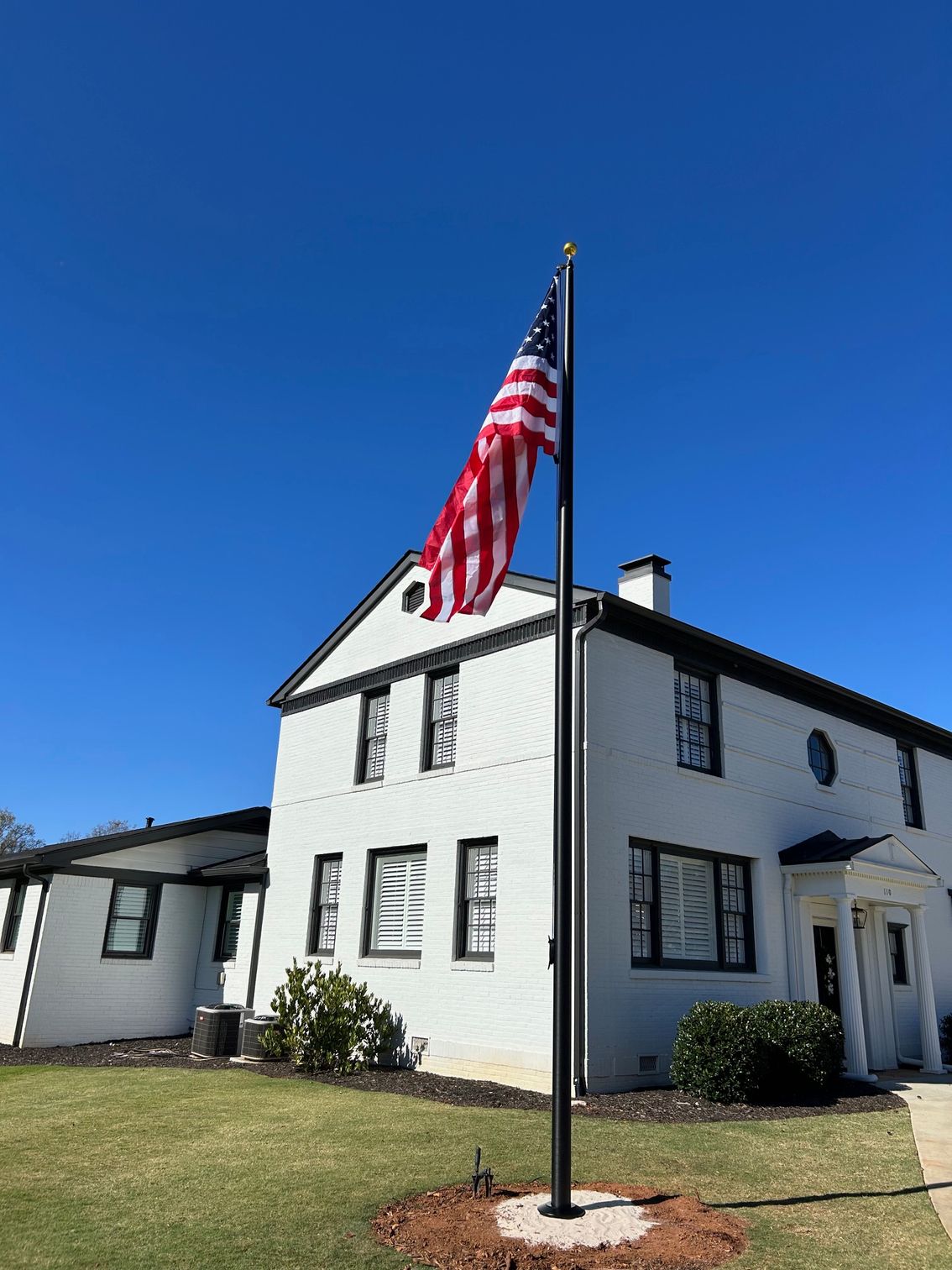 An American flag is waving in the wind against a cloudy blue sky on a black flagpole.