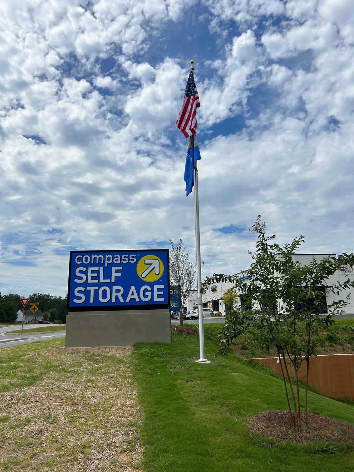 A compass self storage sign with a flag on a pole in front of it.