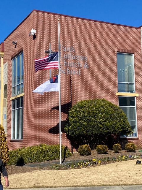 A large brick building with an American and Christian flag being flown at half-staff