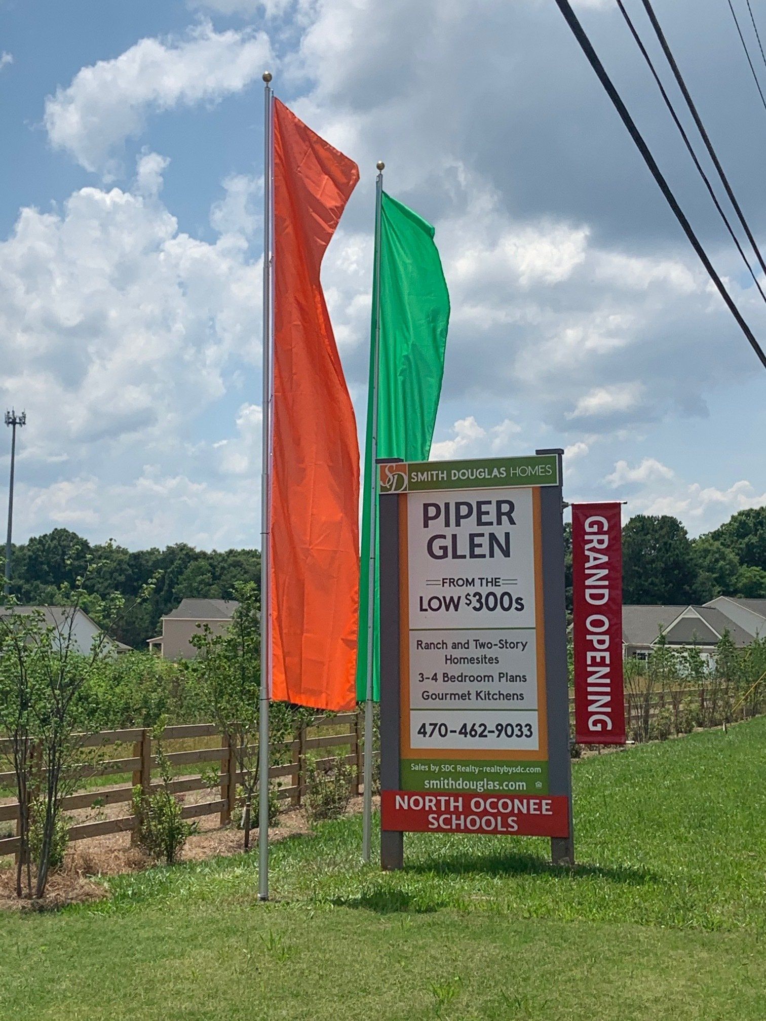 Two flags are flying in front of a sign that says piper glen grand opening.