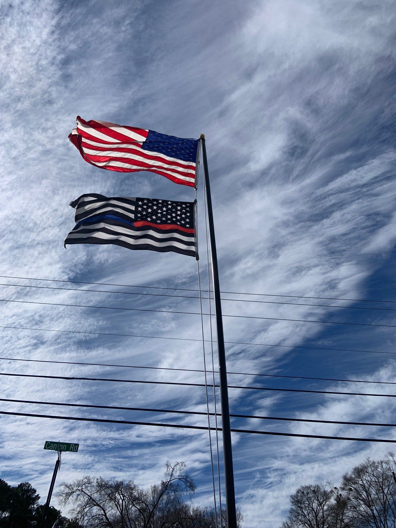 Two american flags are flying in the wind on a pole.