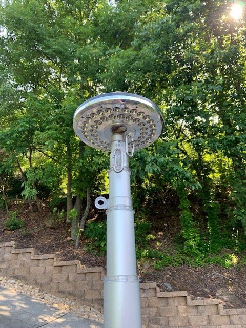 A shower head is sitting on top of a pole in the woods.