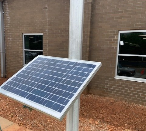 A solar panel is sitting on a pole in front of a brick building.
