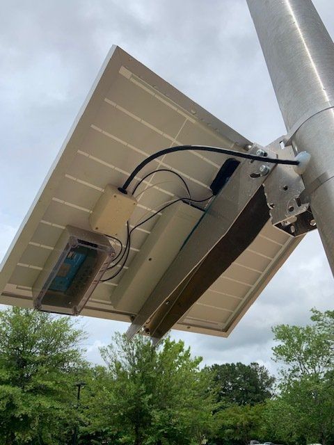A solar panel is attached to a pole with trees in the background