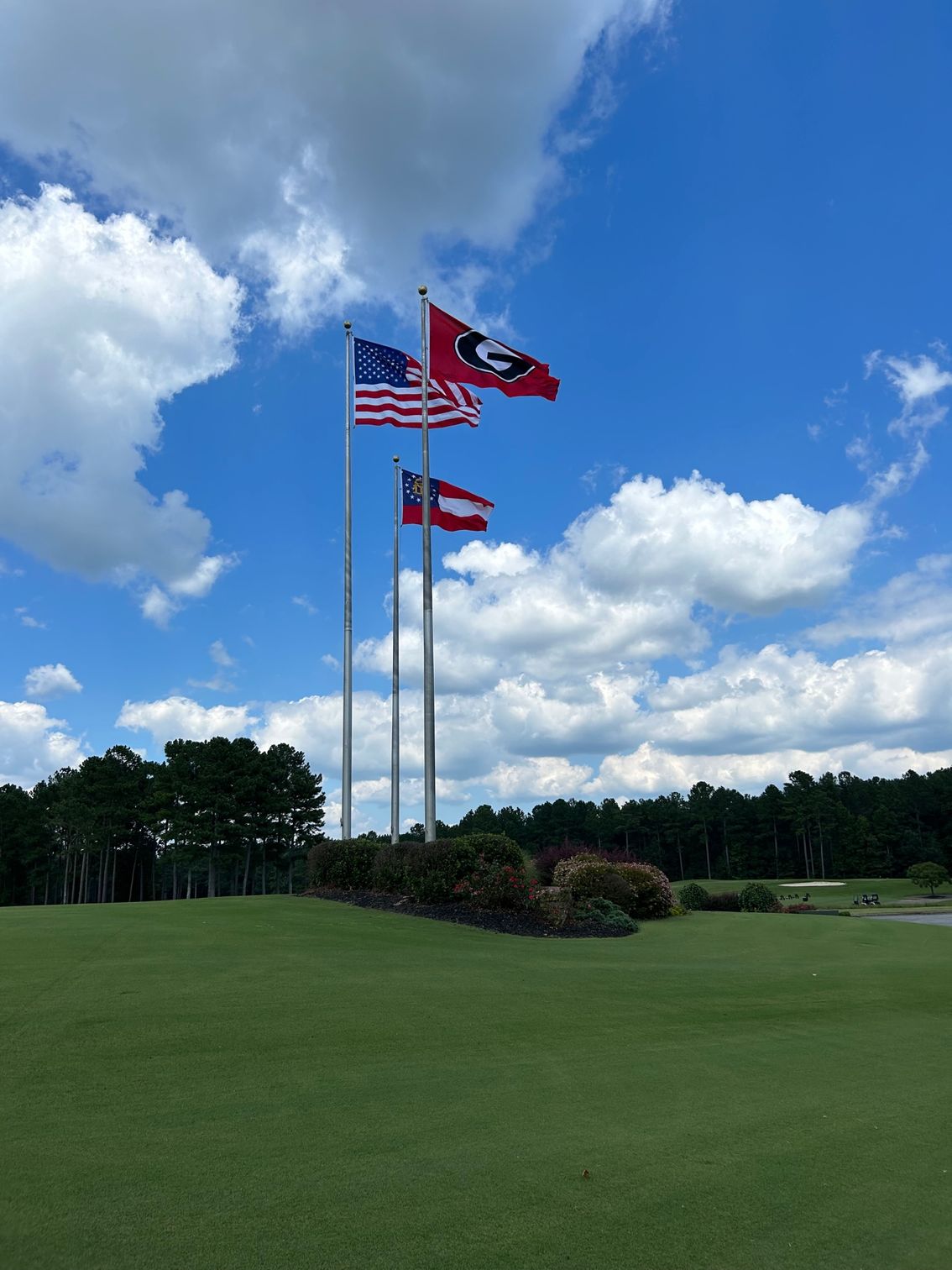Three flags are flying in the wind on a golf course