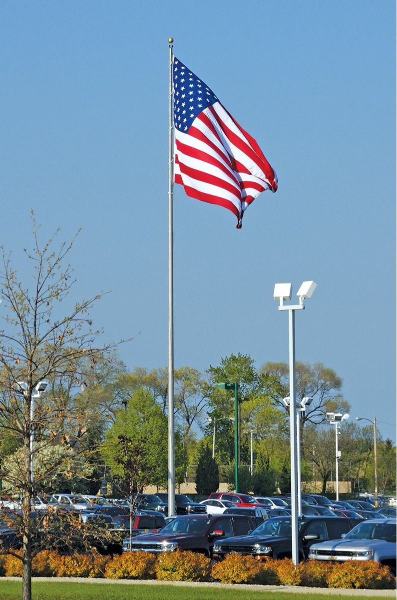 A large american flag is flying in a parking lot