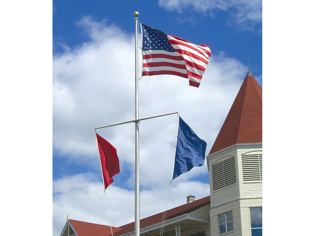 Three flags are flying on a pole in front of a building