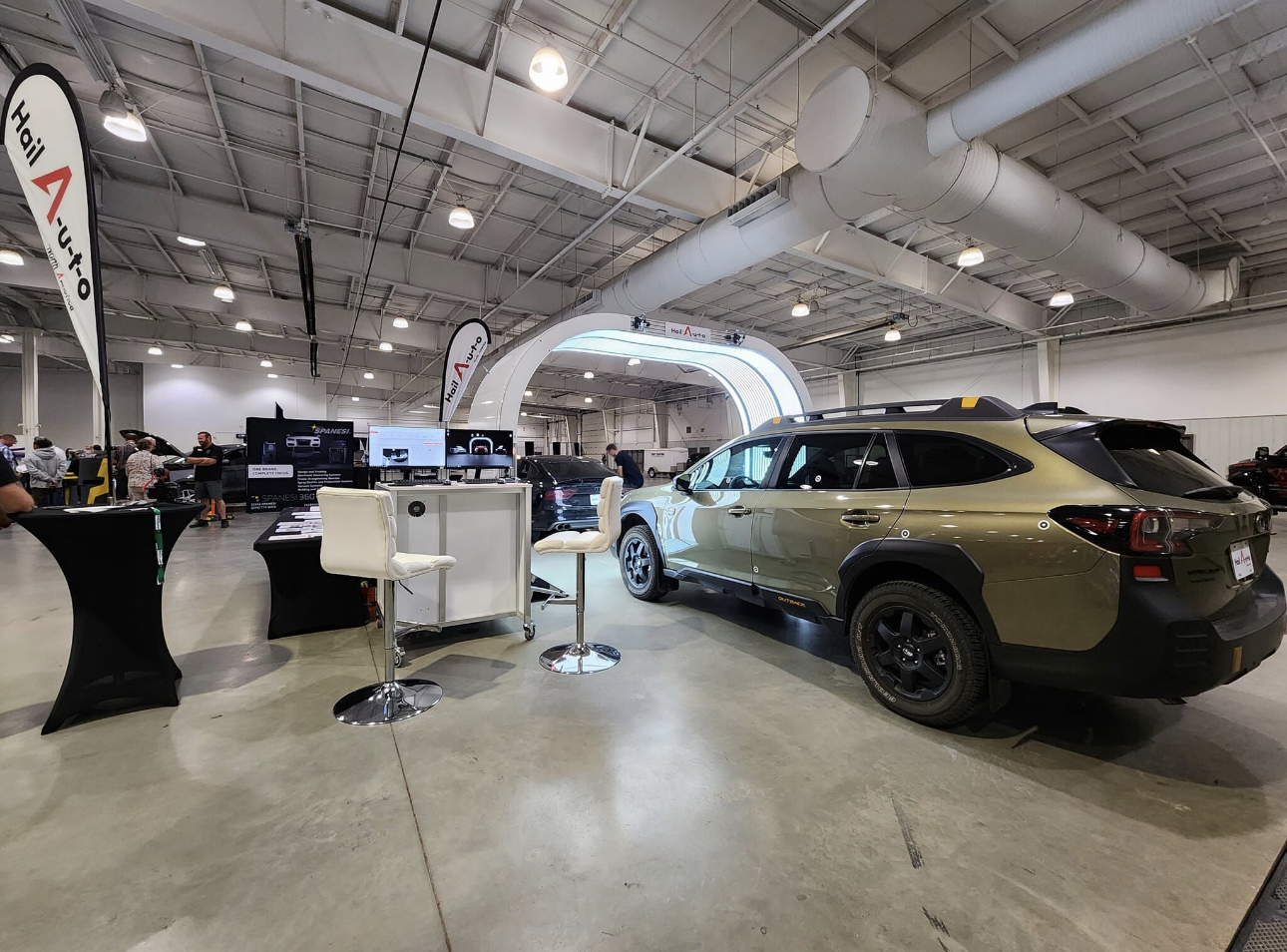 An indoor car show: a green SUV on display with booth and people in an industrial setting.
