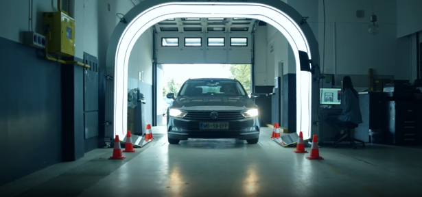 A car drives through a bright, arched inspection scanner in a workshop, with a person operating a computer nearby.