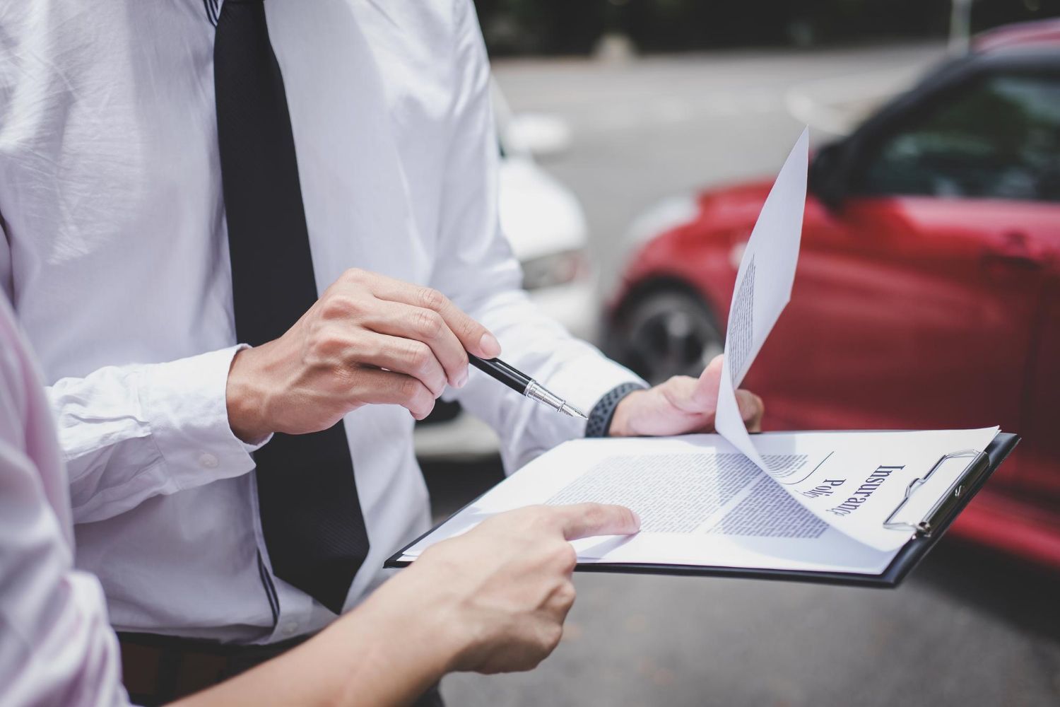 Person pointing at a document on a clipboard, standing by a red car.