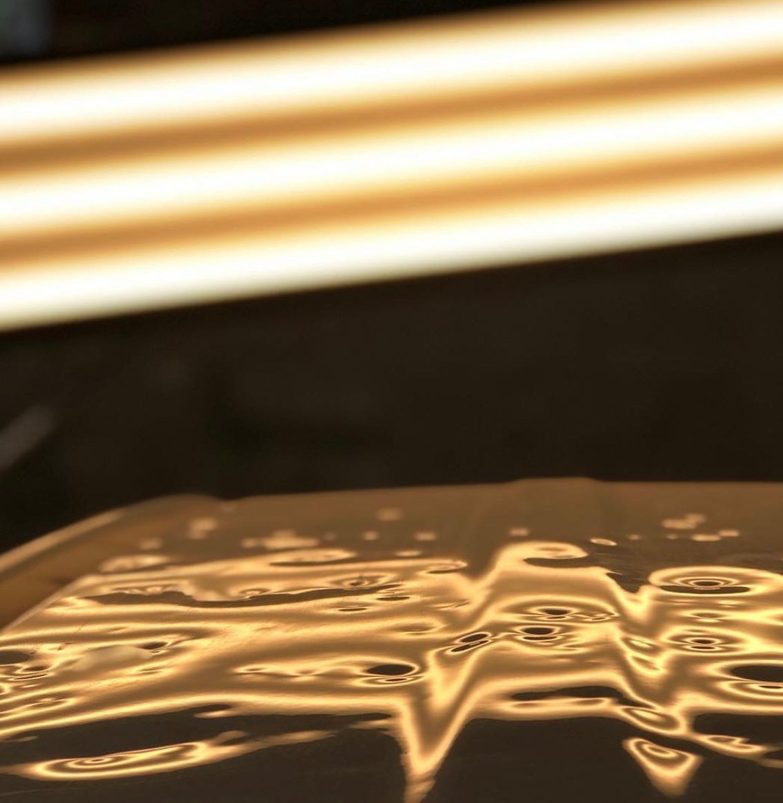 Shiny metal surface with distorted reflections of overhead lighting, hinting at dent repair.