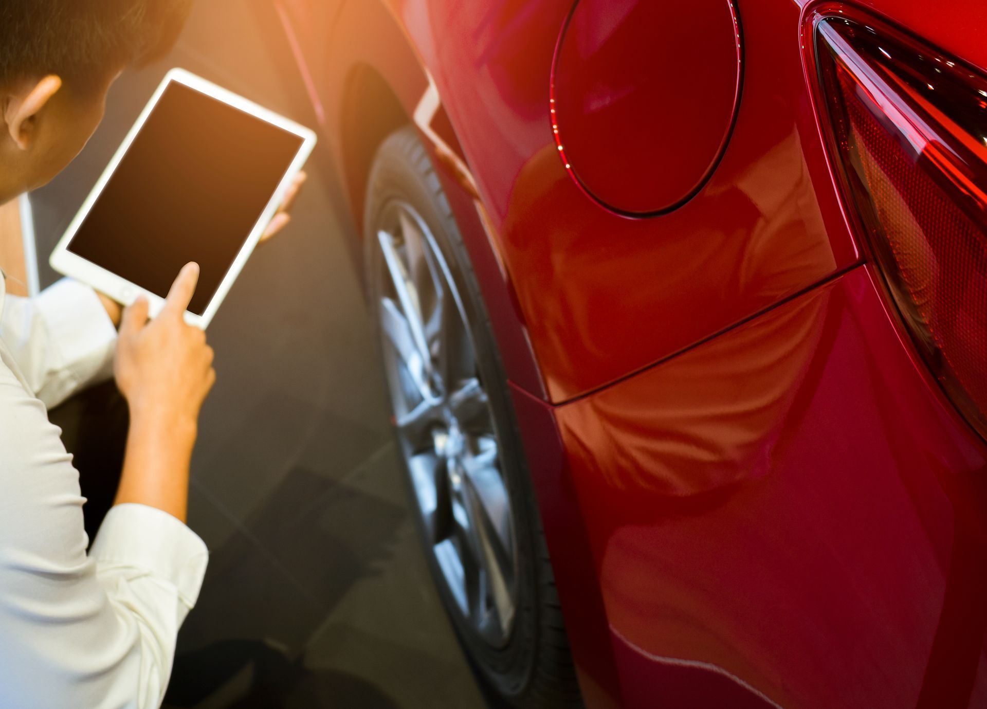 Person holding a tablet near a red car, possibly researching or inspecting it.