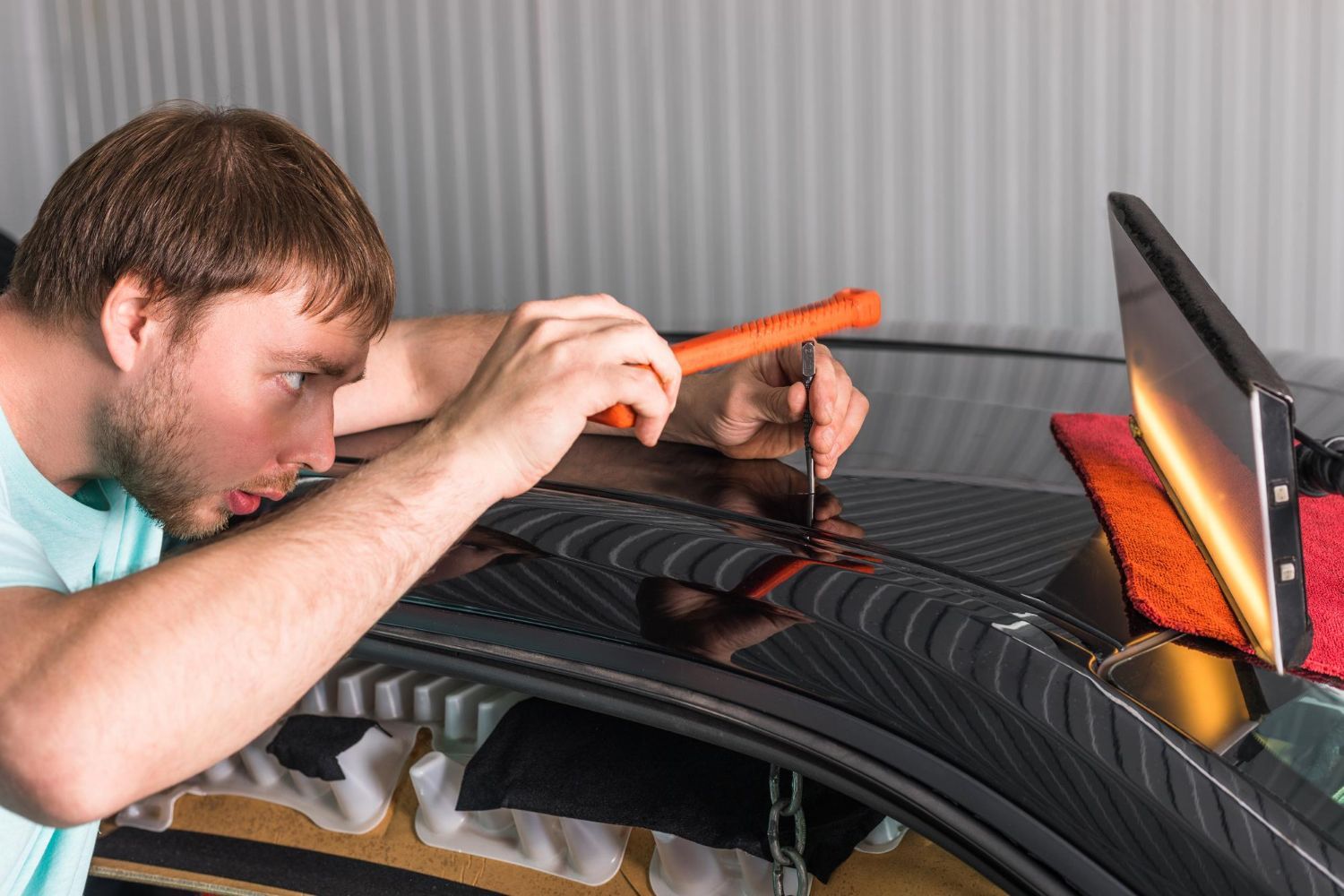 Man repairing car dent on black car roof with tools.