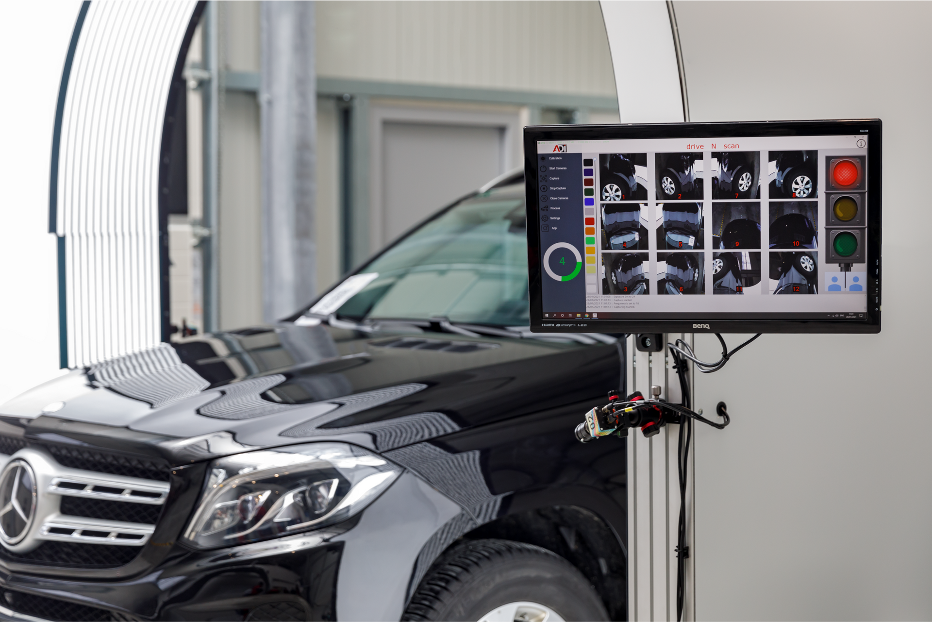 Black car being inspected; a screen displays wheel alignment data in a garage.