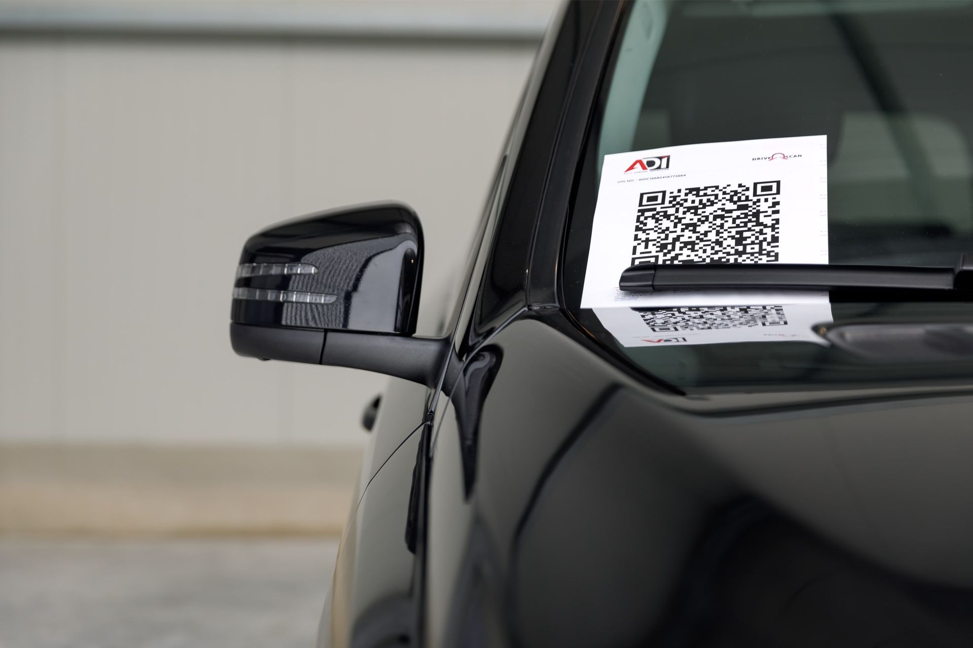 Black car's side mirror and windshield with a ticket holding a QR code.