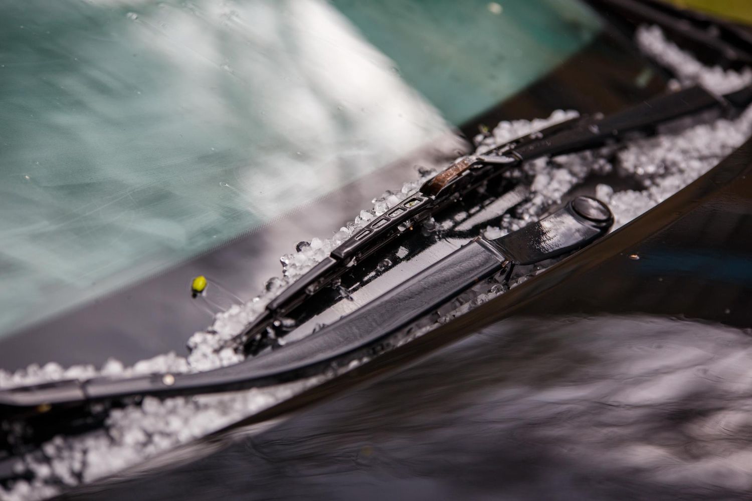 A car windshield covered in scattered hail stones with the black wiper blade resting on the glass.