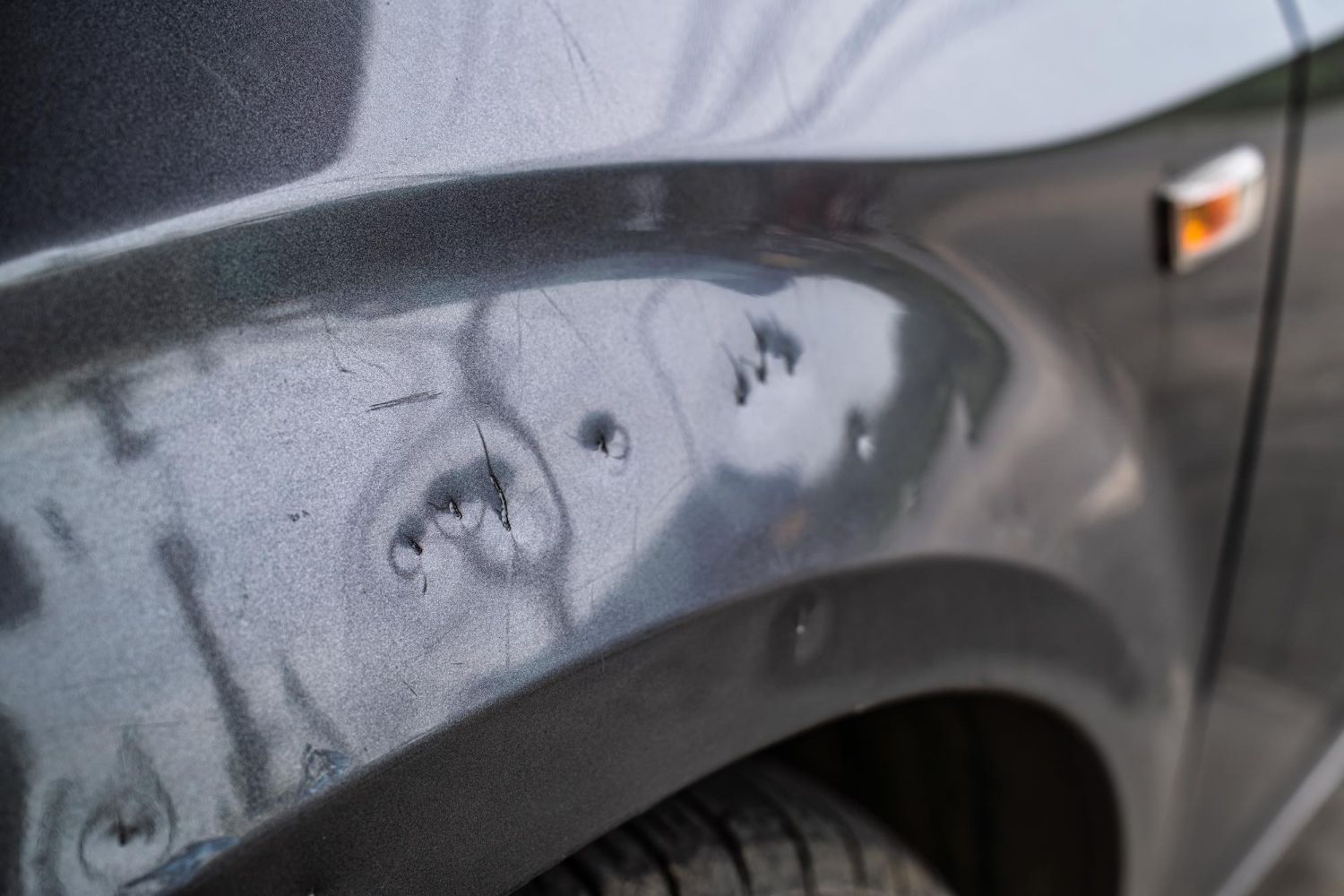 Close-up of a dark grey car fender with multiple small dents and paint damage from hail.