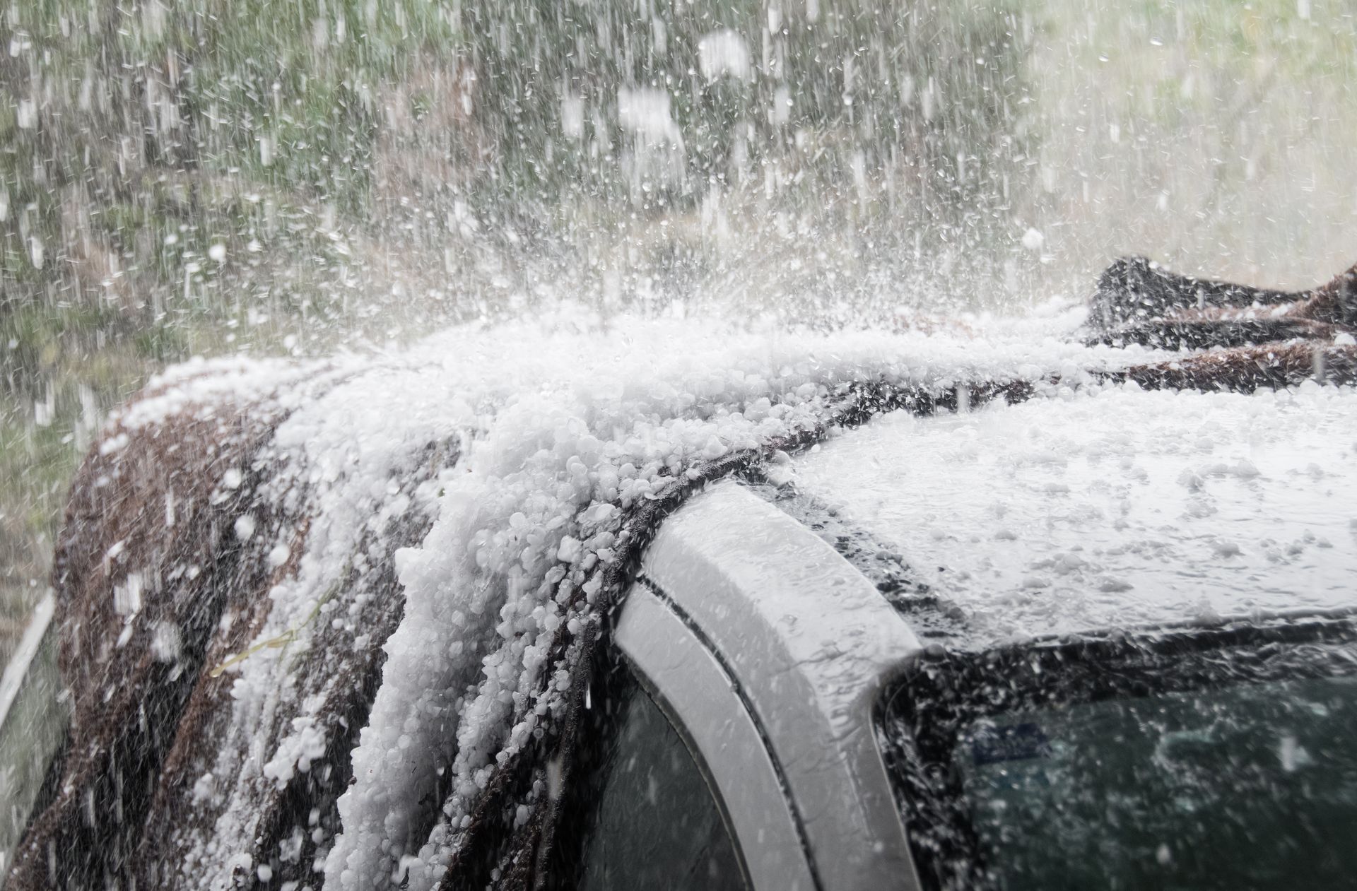 Hail storm covering a car, droplets of hail hitting the roof.