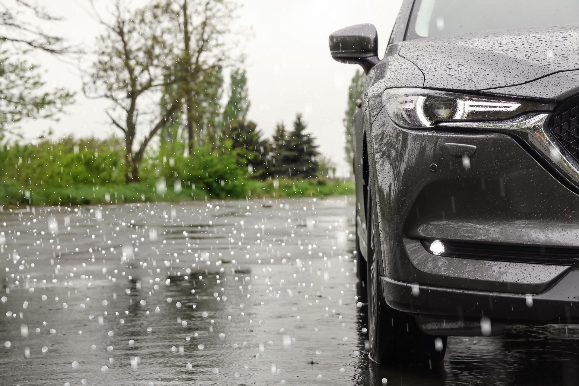 Dark SUV parked on a wet road during a hailstorm, with trees in the background.