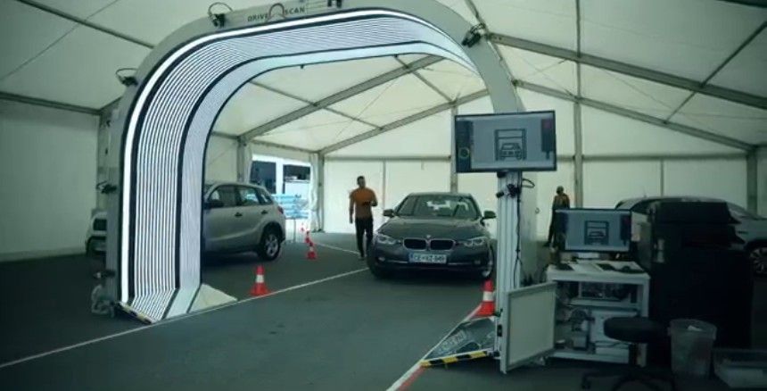 Cars drive through an inspection archway. People monitor screens in a tent.