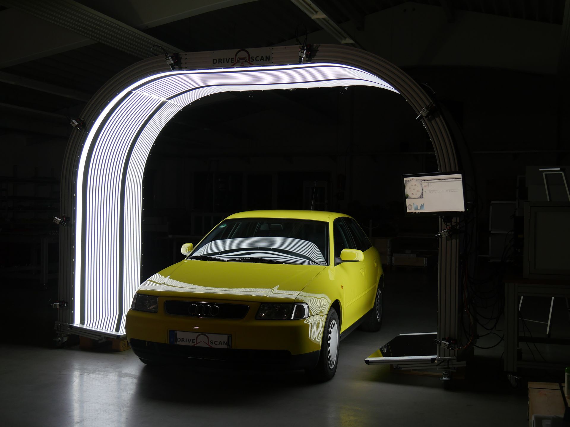 Yellow car inside a structure with white lights; an inspection setting.