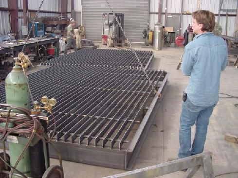 A man in a blue shirt is standing in front of a large piece of metal.