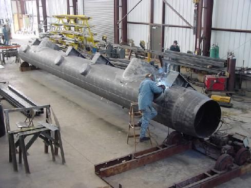 A man is welding a large pipe in a factory.