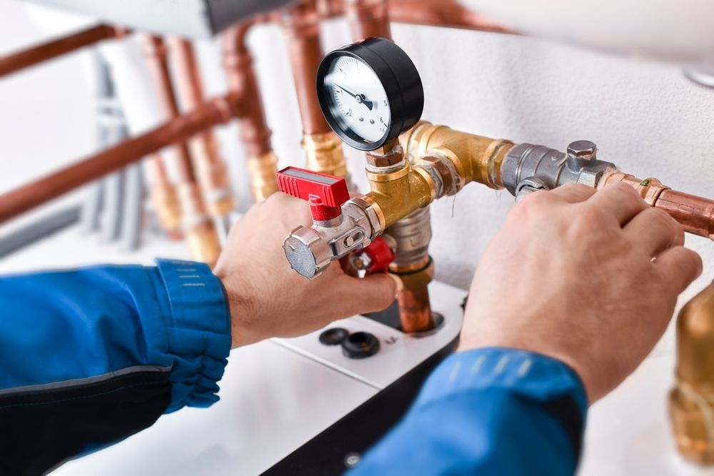 A technician in a blue uniform checks the pressure gauge and valves on a copper piping system.