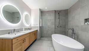 A modern bathroom with a wood vanity, two round backlit mirrors, a freestanding white tub, and a glass-enclosed shower.