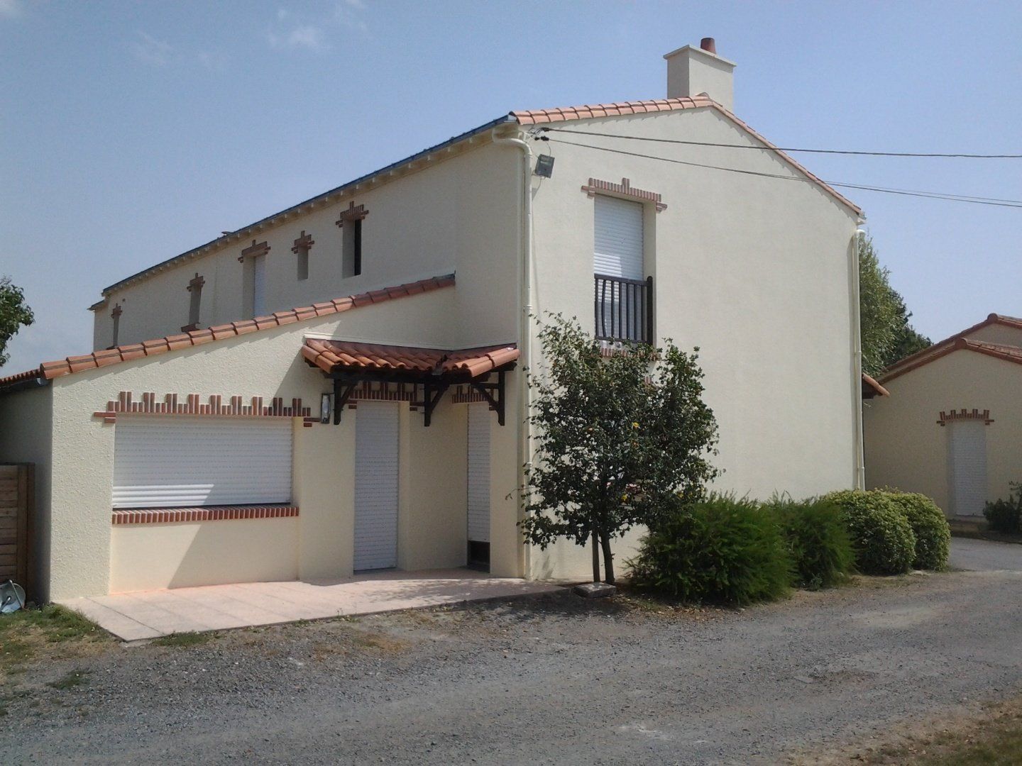 Une maison blanche avec un toit de tuiles rouges et des volets aux fenêtres
