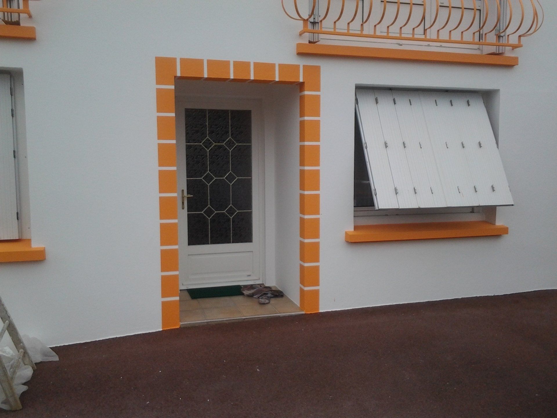 Une maison blanche avec des bordures orange a une porte et une fenêtre