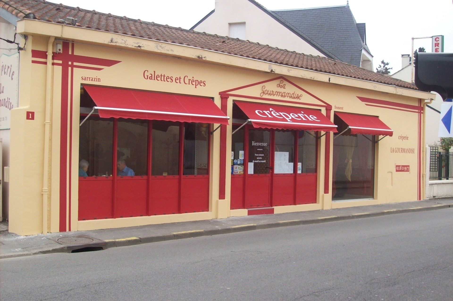 Un bâtiment jaune avec des auvents rouges porte le mot café