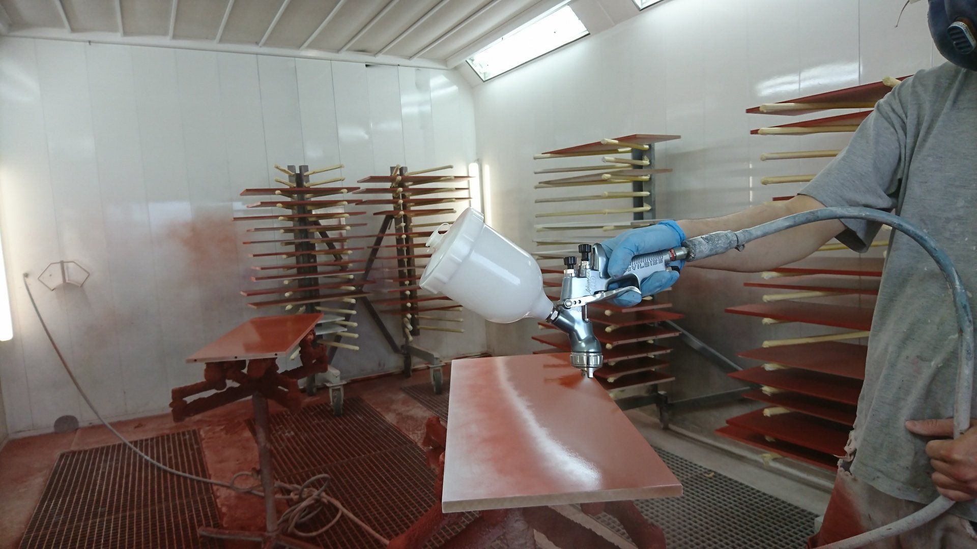 Un homme peint au pistolet un morceau de bois dans une cabine de peinture.