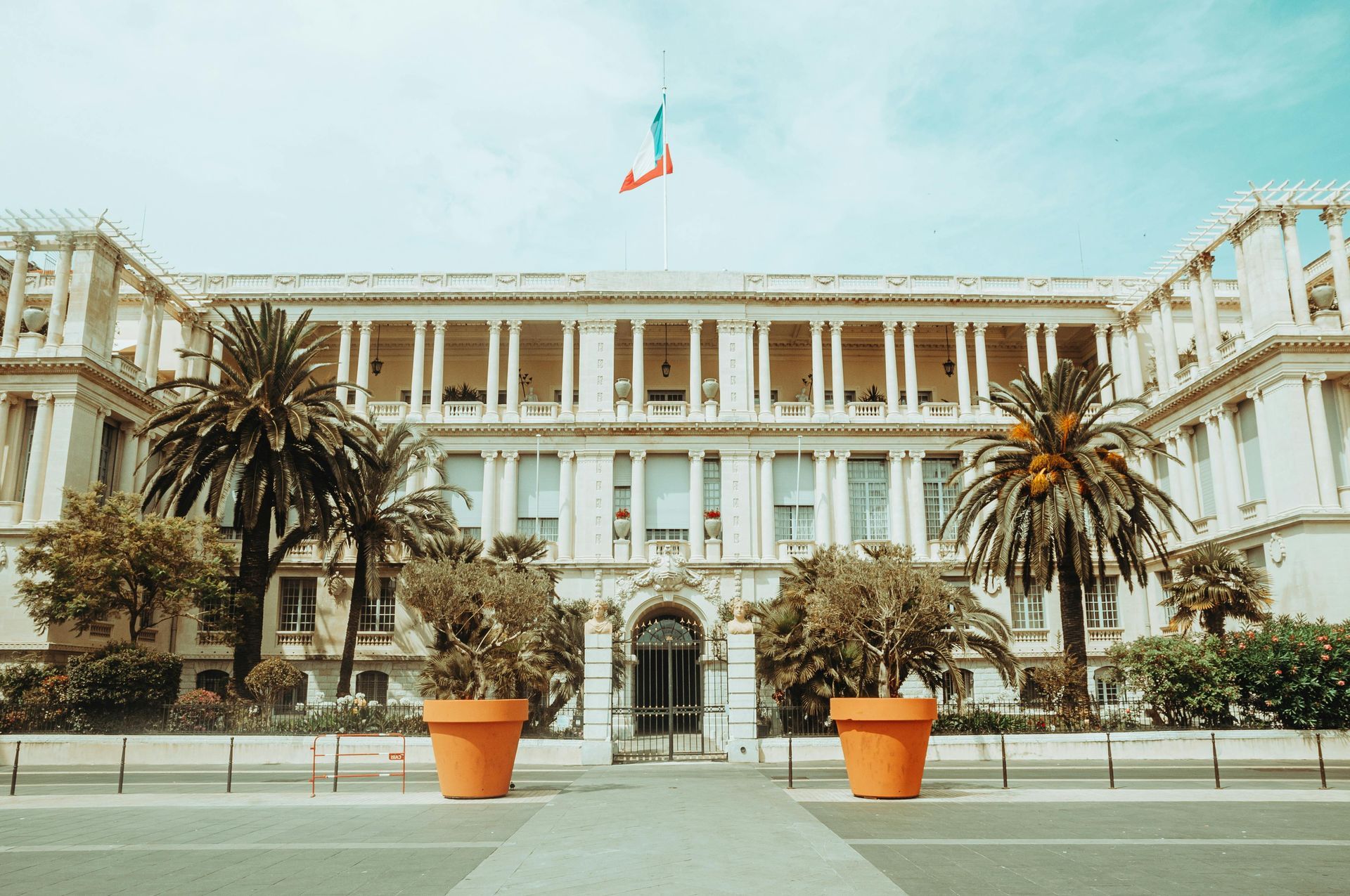 Élégant bâtiment blanc à colonnes, orné d'un drapeau français, flanqué de palmiers et de grands pots d'orangers.