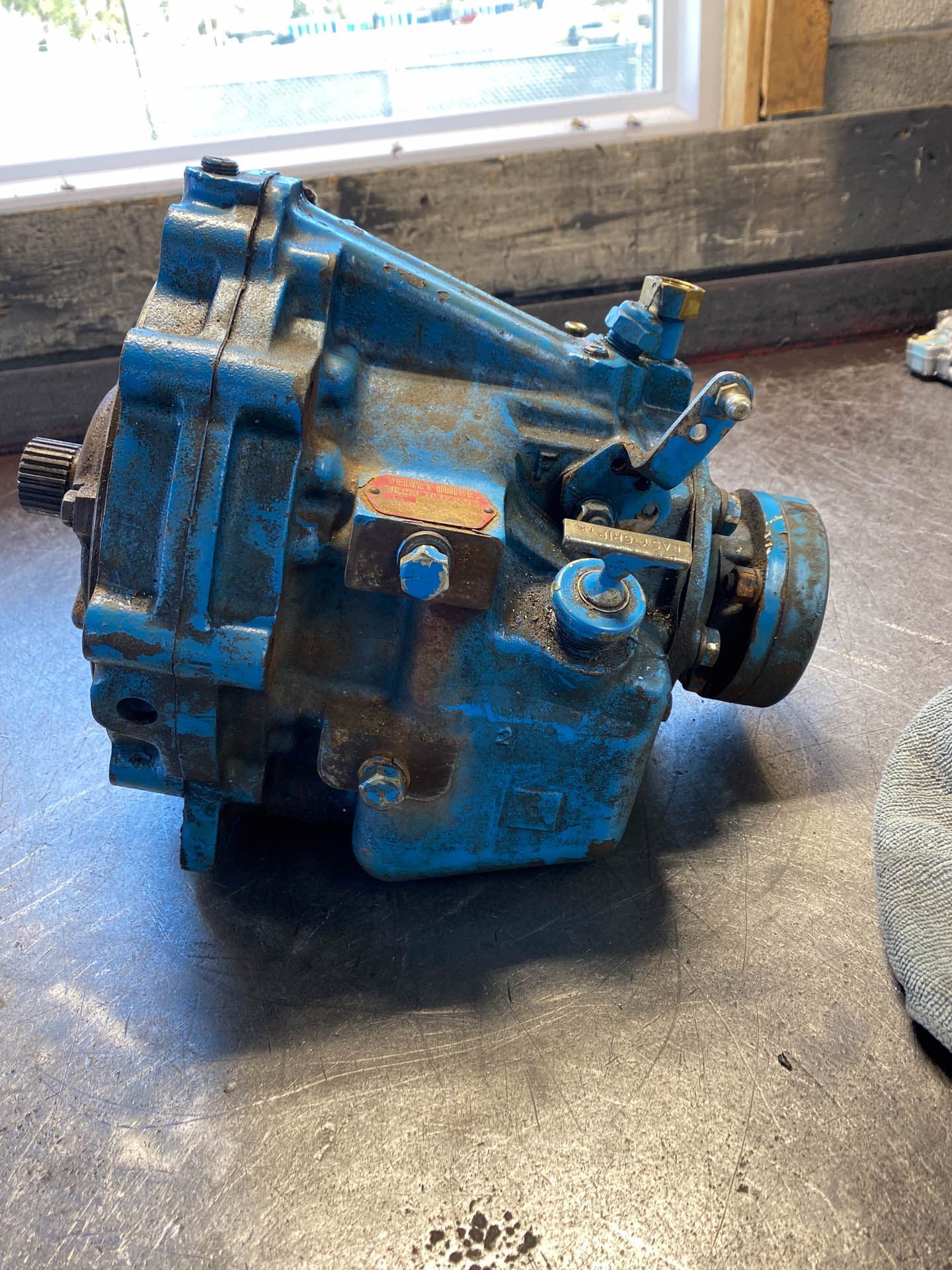 A blue gearbox is sitting on a table next to a window.