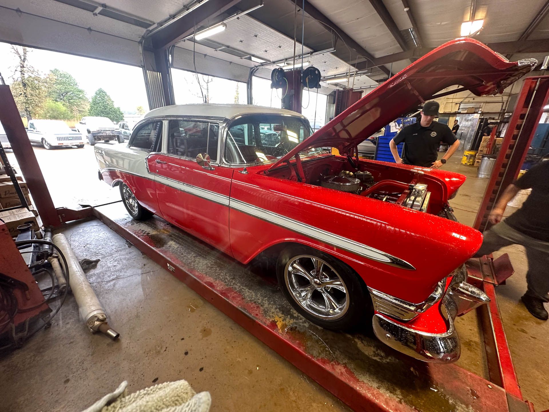 A red and white car with the hood up is on a lift in a garage.