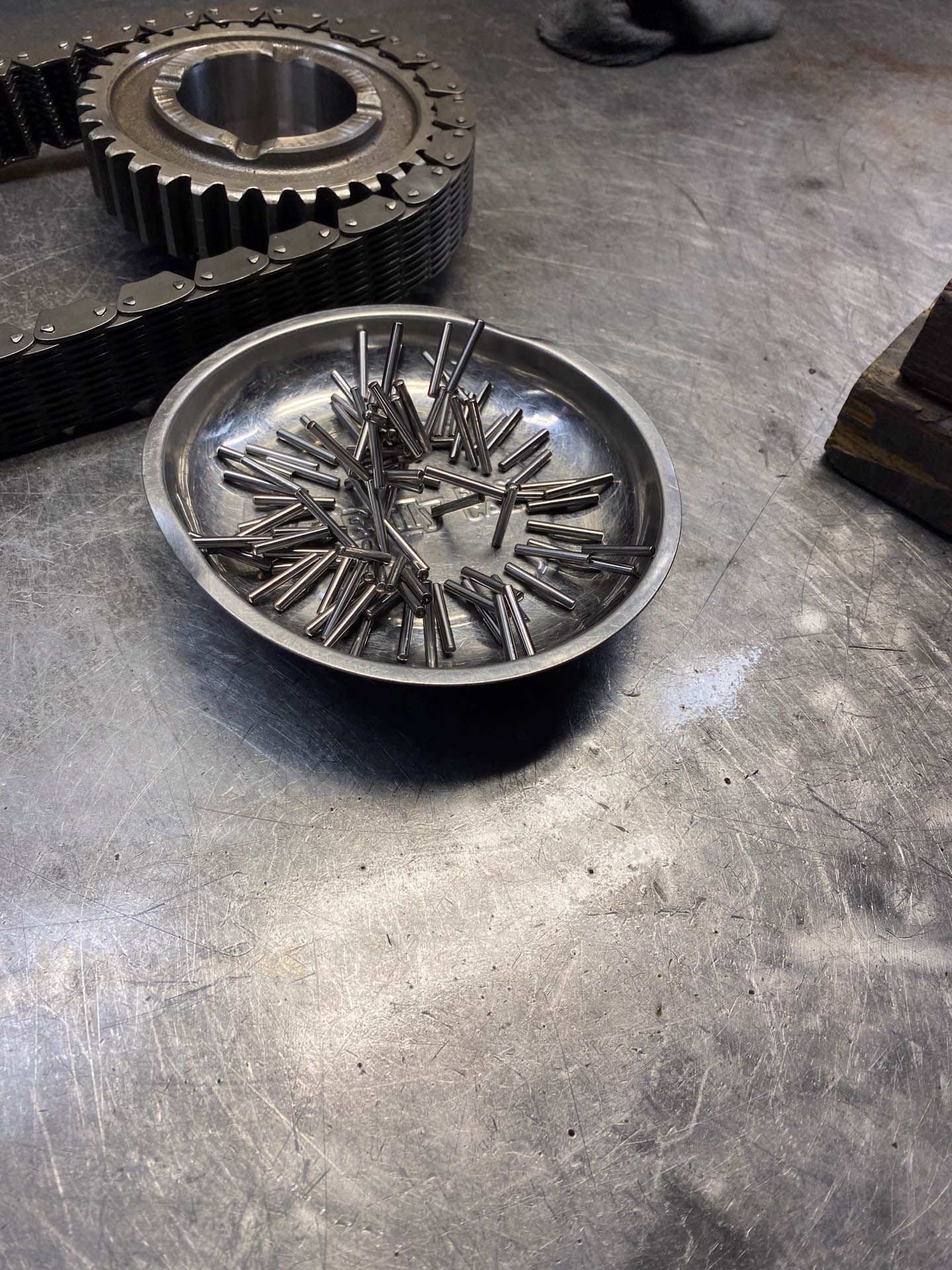 A metal tray filled with nails is sitting on a table next to a gear.