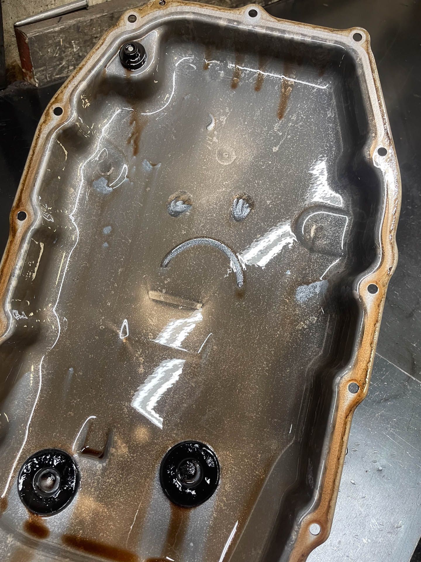 A dirty oil pan with a sad face on it