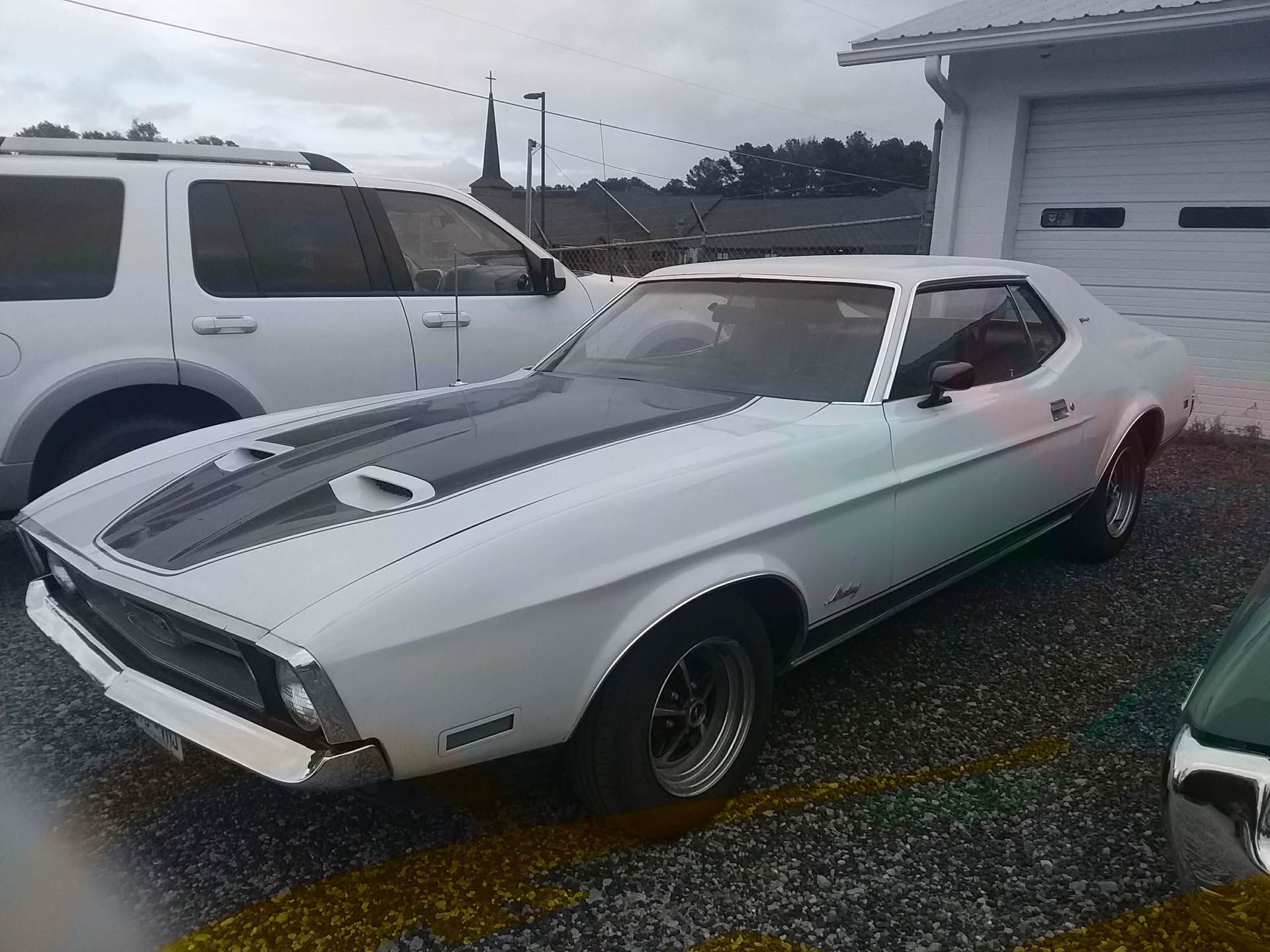 A white mustang is parked in front of a garage