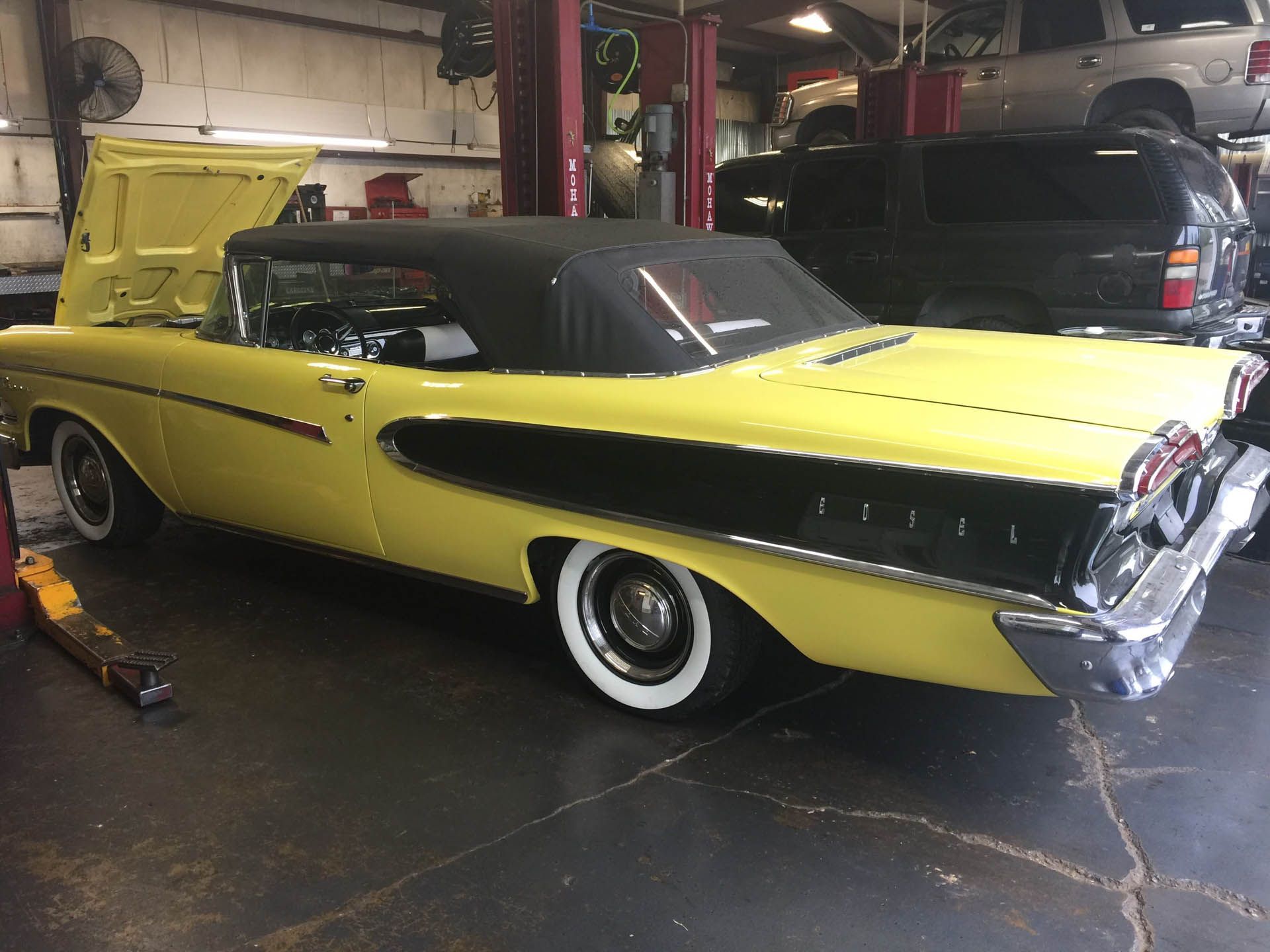 A yellow car is parked in a garage with the hood up.